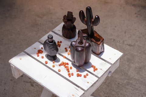 Dark wooden artisanal chiltepin grinders and scattered orange chiltepin peppers on a distressed wooden table